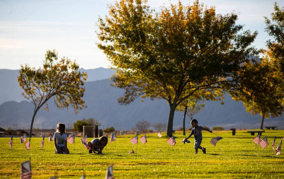 Enoch Ayala, 2, of Boulder City, runs with a flag as volunteers place American flags on graves ...