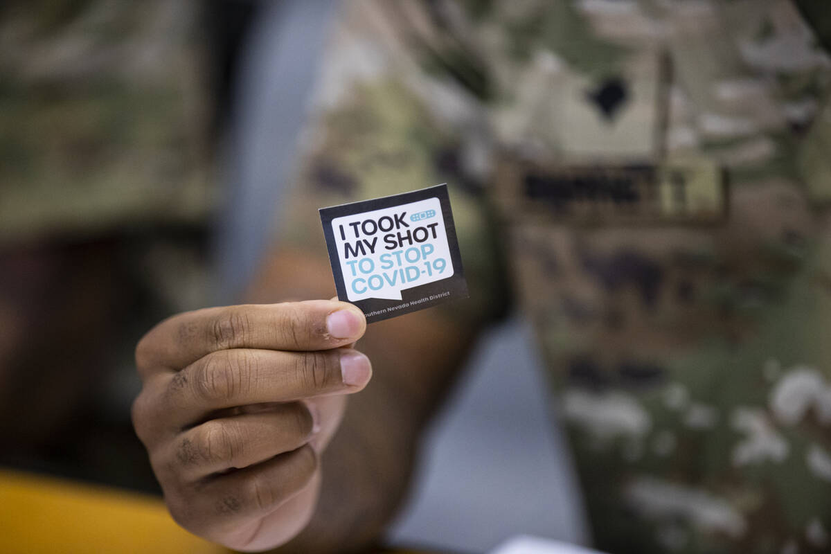 Nevada National Guard Spc. Demetrie Barnett holds up a sticker at his station at the vaccinatio ...