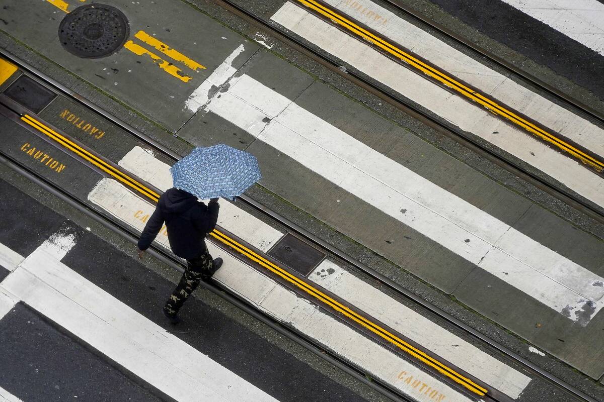 A pedestrian carries an umbrella while crossing a street in San Francisco, Monday, Dec. 13, 202 ...