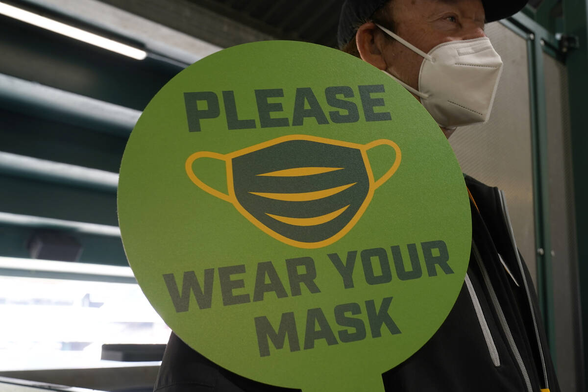 A stadium worker holds up a sign for people to wear face masks before a game between the Oaklan ...