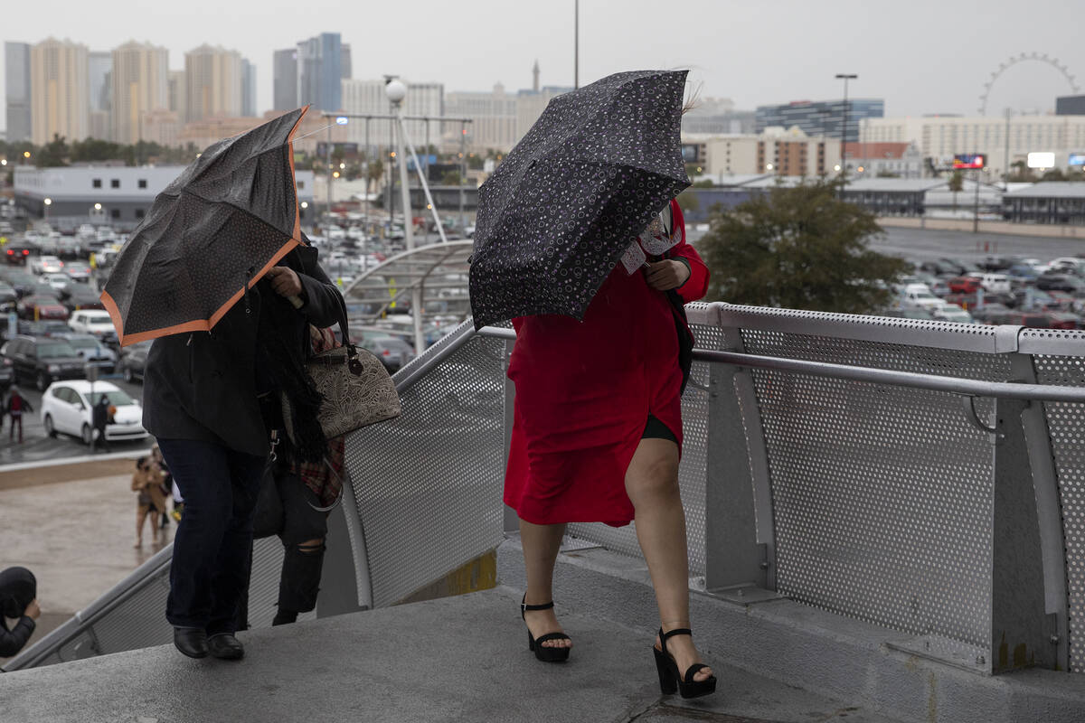 UNLV graduates shield themselves from wind and rain as they walk into their graduation ceremony ...