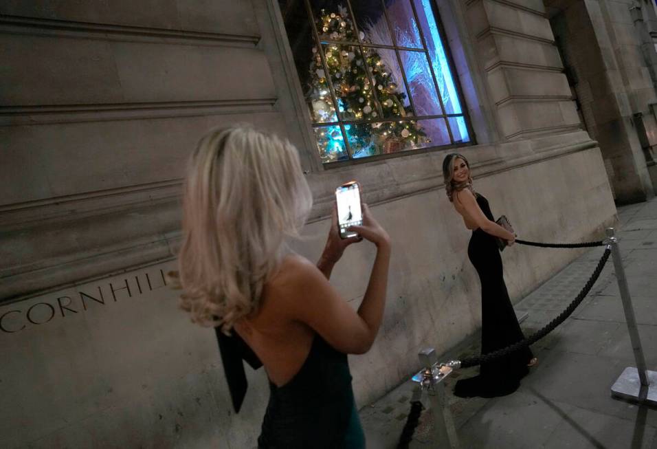 Two women dressed for a party take photos of each other outside a venue in London, Friday, Dec. ...
