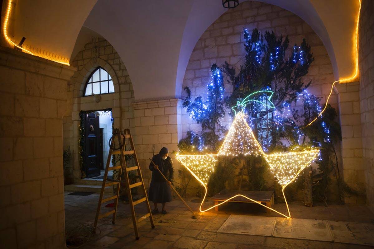 A nun cleans the floor after decorating the entrance to a church with Christmas lights, in Jeru ...