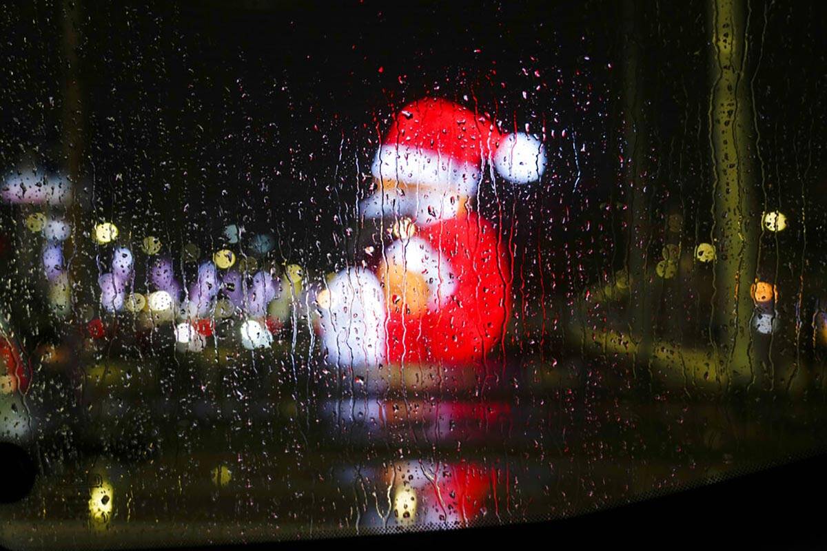 Rain drops on a car window are backdropped by city lights and a giant lit figure of Santa Claus ...