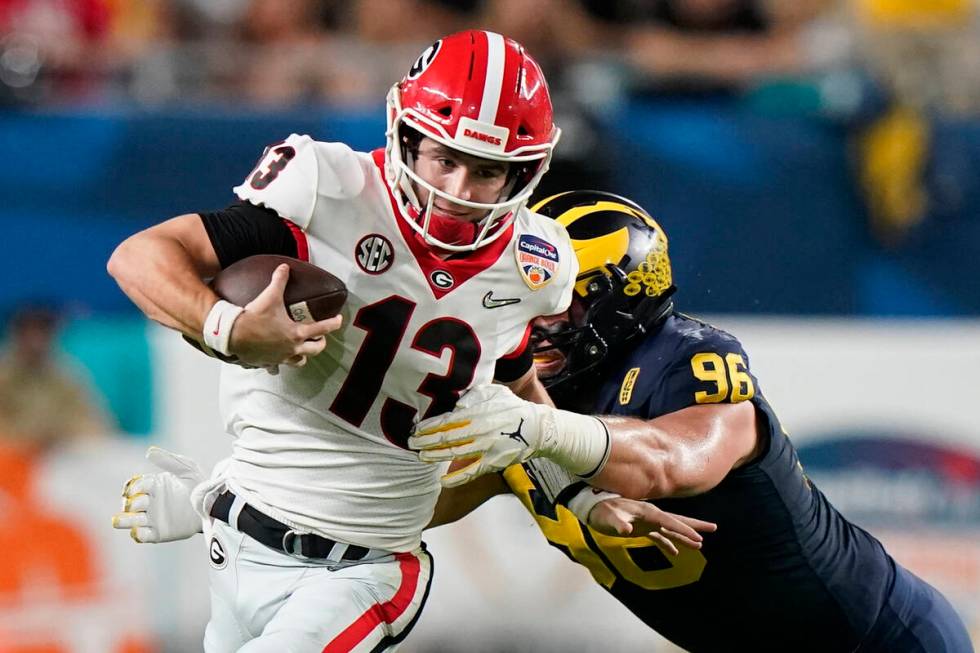 Georgia quarterback Stetson Bennett breaks away from Michigan defensive lineman Julius Welschof ...