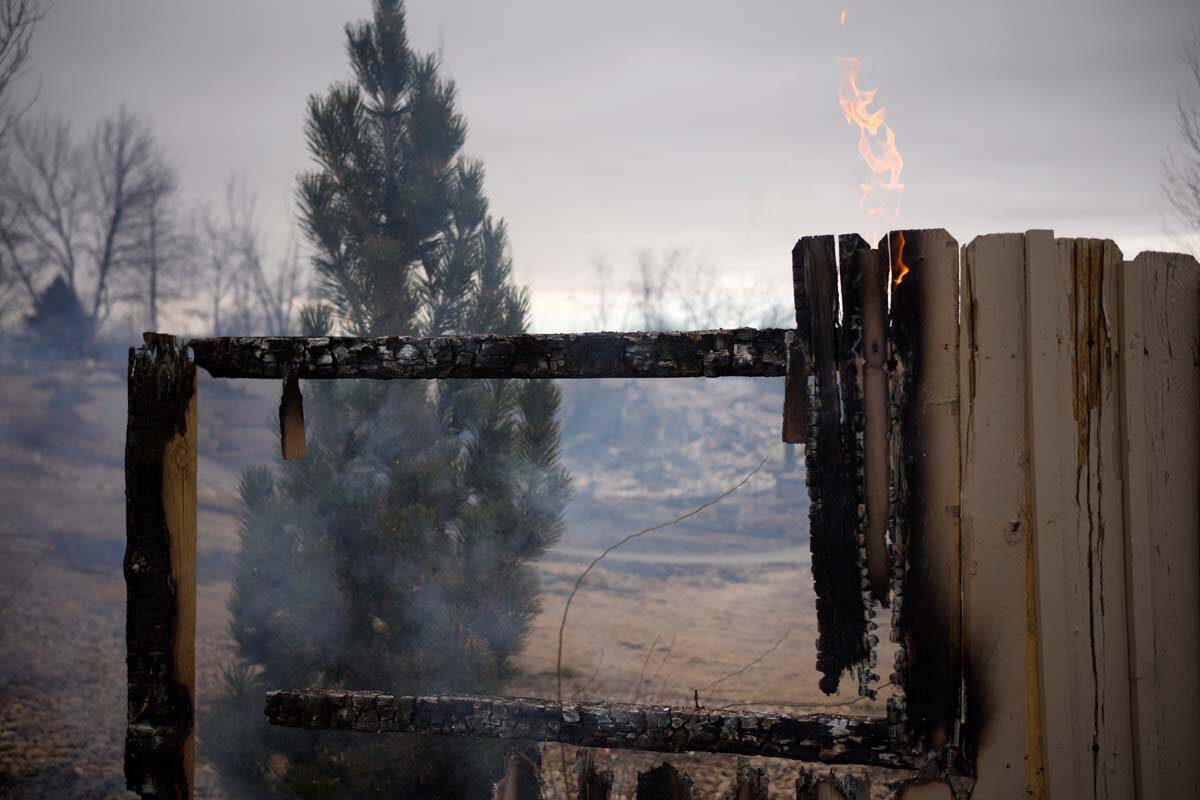 Flames leap from a fence near the remains of homes burned by wildfires after they ripped throug ...