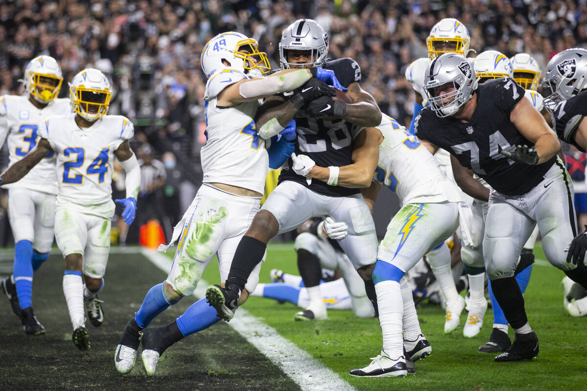 Raiders running back Josh Jacobs (28) runs for a touchdown under pressure from Los Angeles Char ...