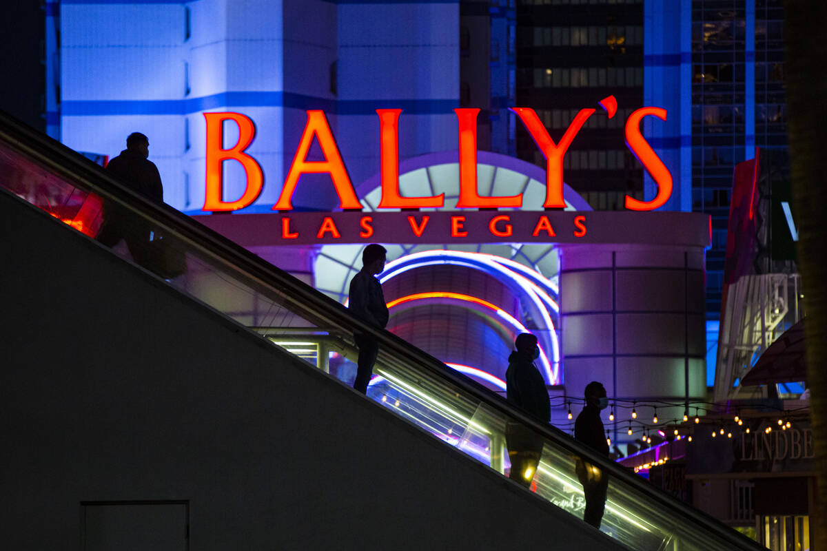 People are silhouetted by a sign for Bally's as they descend an escalator from a pedestrian bri ...