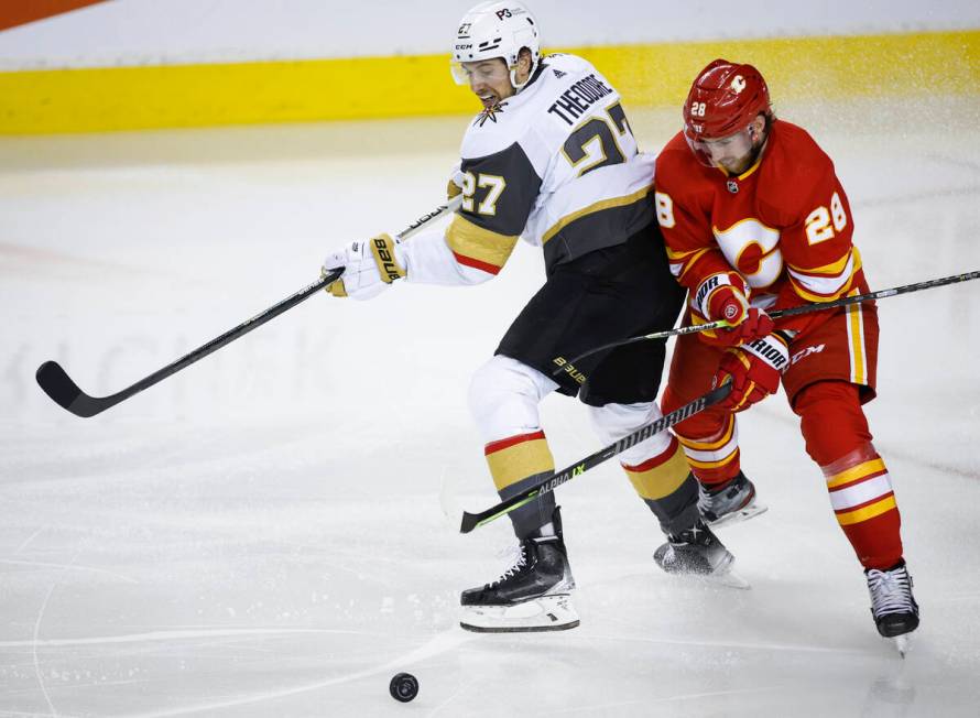 Vegas Golden Knights' Shea Theodore, left, and Calgary Flames' Elias Lindholm chase the puck du ...