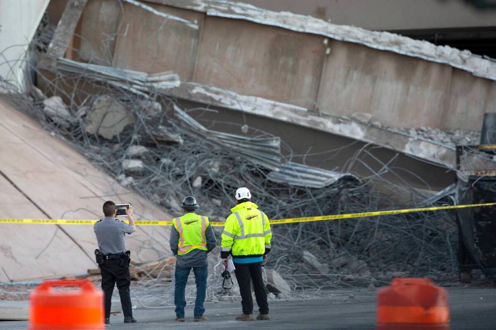 A Las Vegas police officer and Las Vegas Paving Corp. employees survey the damage after a porti ...