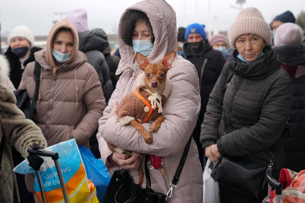 A woman holds her dog as she waits with others to cross from Ukrainian government controlled ar ...