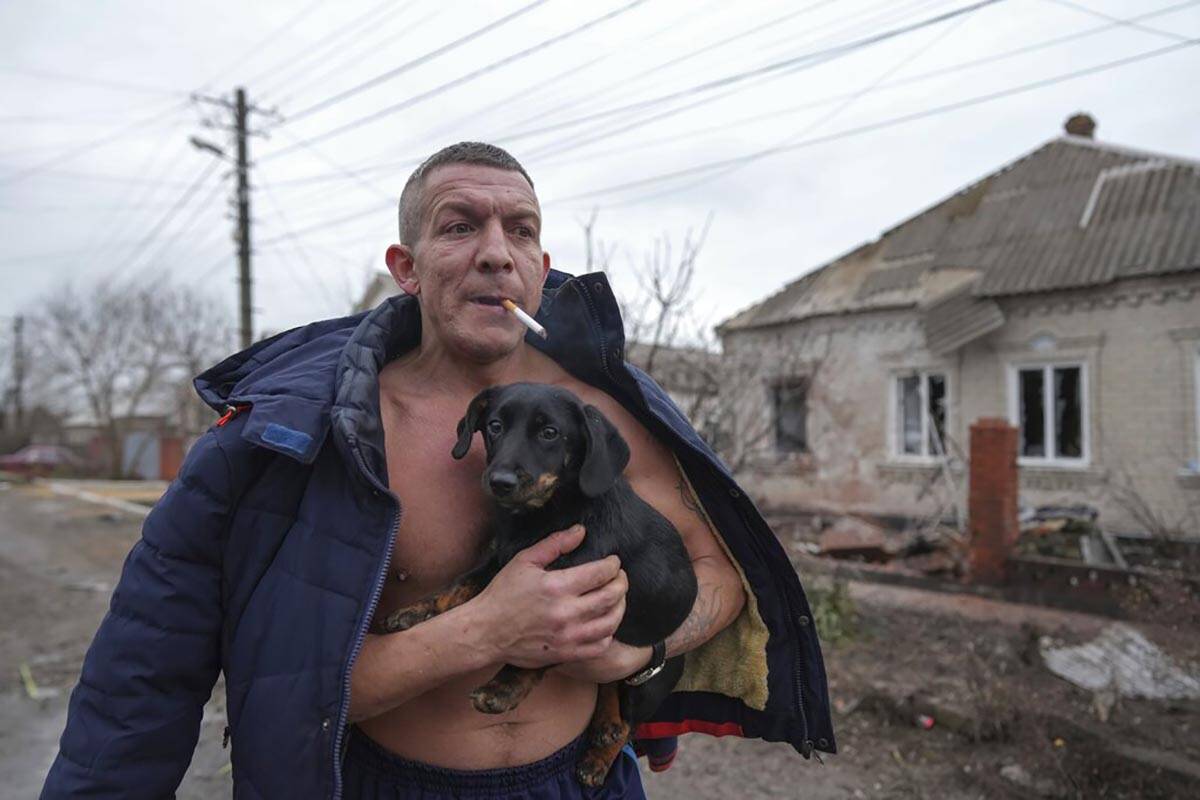 A man holds a dog as he walks past a damaged house following Russian shelling, in Mariupol, Ukr ...
