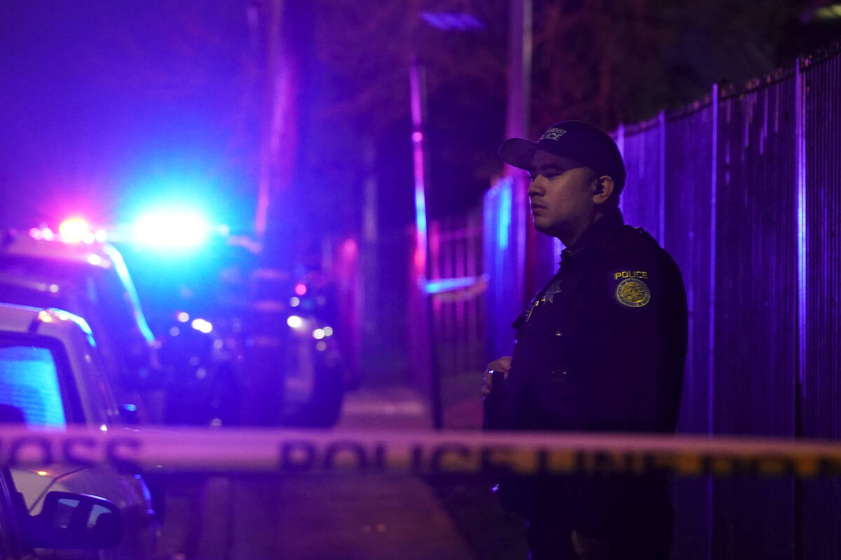 A Sacramento Police officer stands behind police tape blocking the street near the scene of a s ...