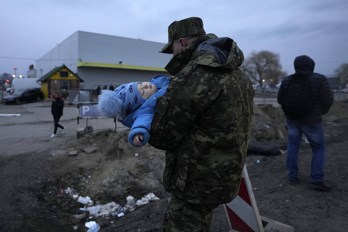 A Polish soldier carries a baby of a Ukrainian refugee upon their arrival at the border crossin ...