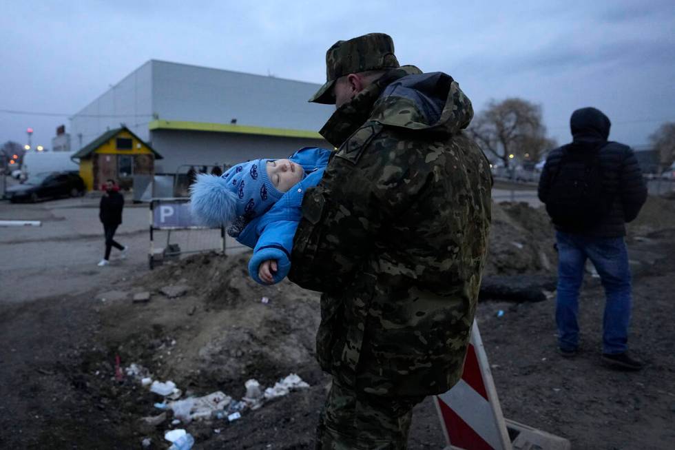 A Polish soldier carries a baby of a Ukrainian refugee upon their arrival at the border crossin ...