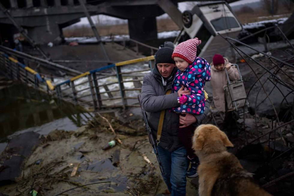 Local militiaman Valery, 37, carries a child as he helps a fleeing family across a destroyed br ...