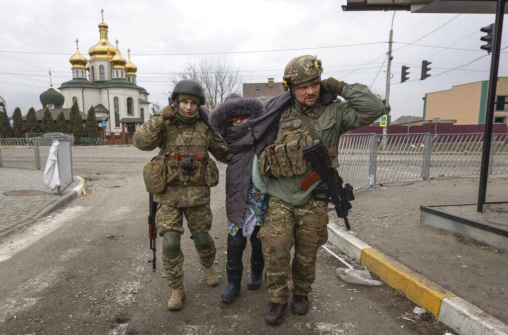 Ukrainian servicemen help an elderly woman, in the town of Irpin, Ukraine, Sunday, March 6, 202 ...