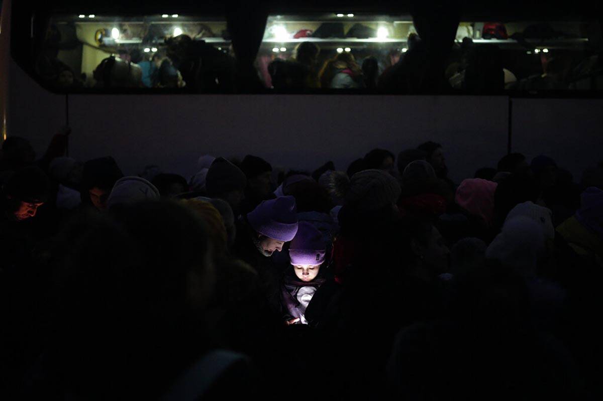 The faces of refugees fleeing the war in Ukraine are illuminated by the light from a phone as t ...