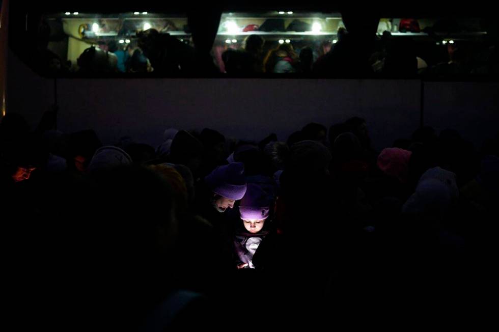 The faces of refugees fleeing the war in Ukraine are illuminated by the light from a phone as t ...