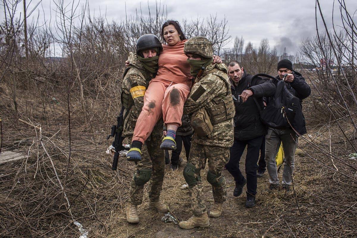 A woman carried by Ukrainian soldiers crosses an improvised path while fleeing the town of Irpi ...