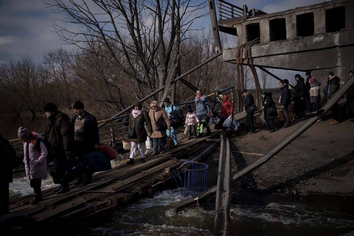 Ukrainians cross an improvised path under a destroyed bridge while fleeing Irpin, on the outski ...