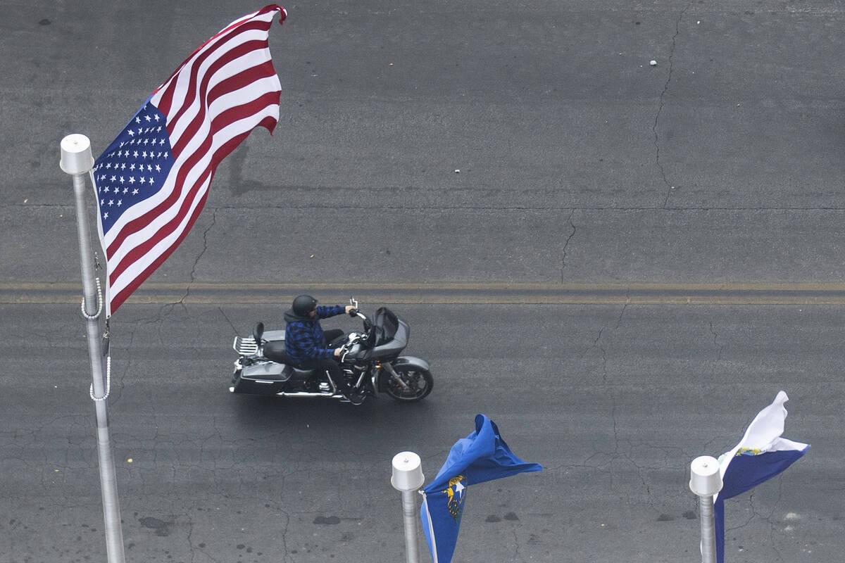 A motorcyclist rides past the Regional Justice Center as strong wind blows flags on Thursday, M ...