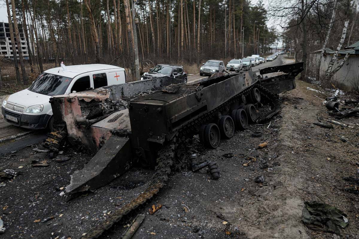 Cars drive past a destroyed Russian tank as a convoy of vehicles evacuating civilians leaves Ir ...