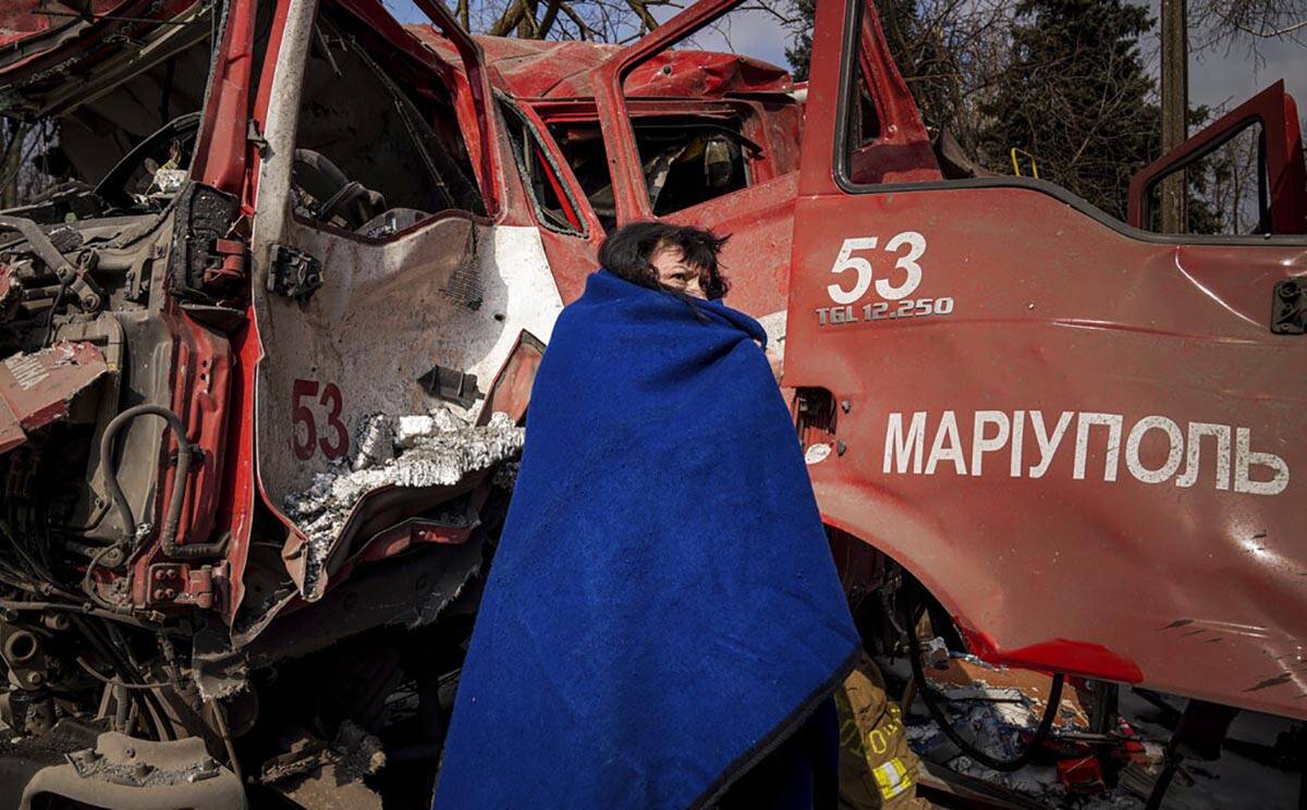 A women covers herself with a blanket near a damaged fire truck after shelling in Mariupol, Ukr ...