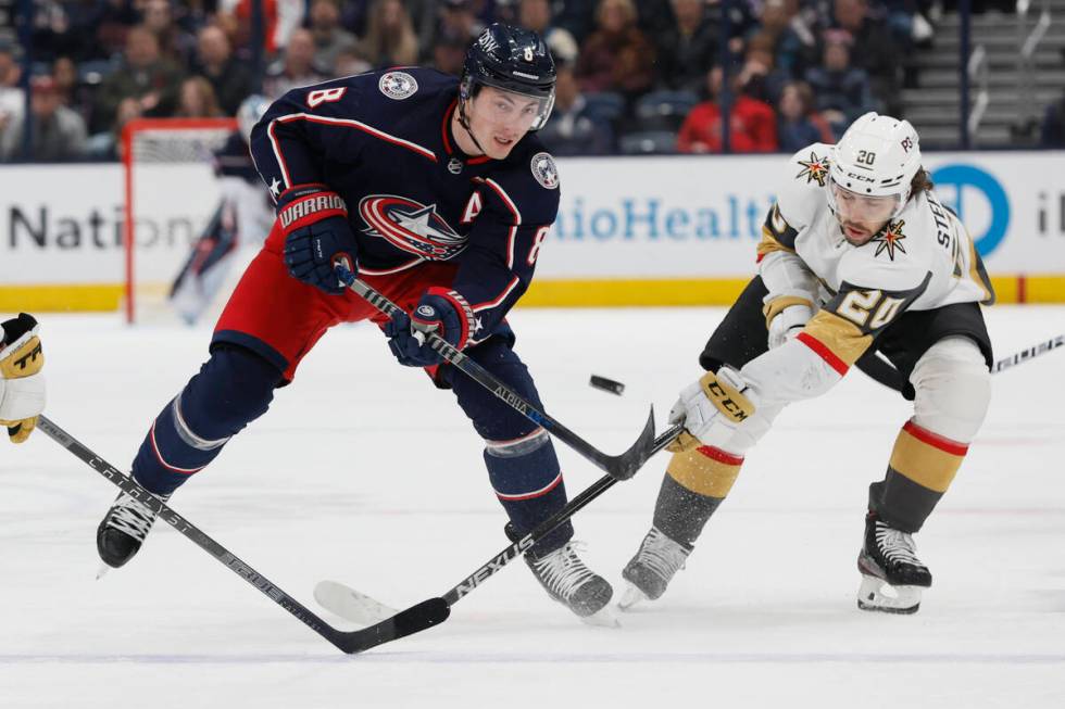 Columbus Blue Jackets' Zach Werenski, left, dumps the puck across the blue line as Vegas Golden ...