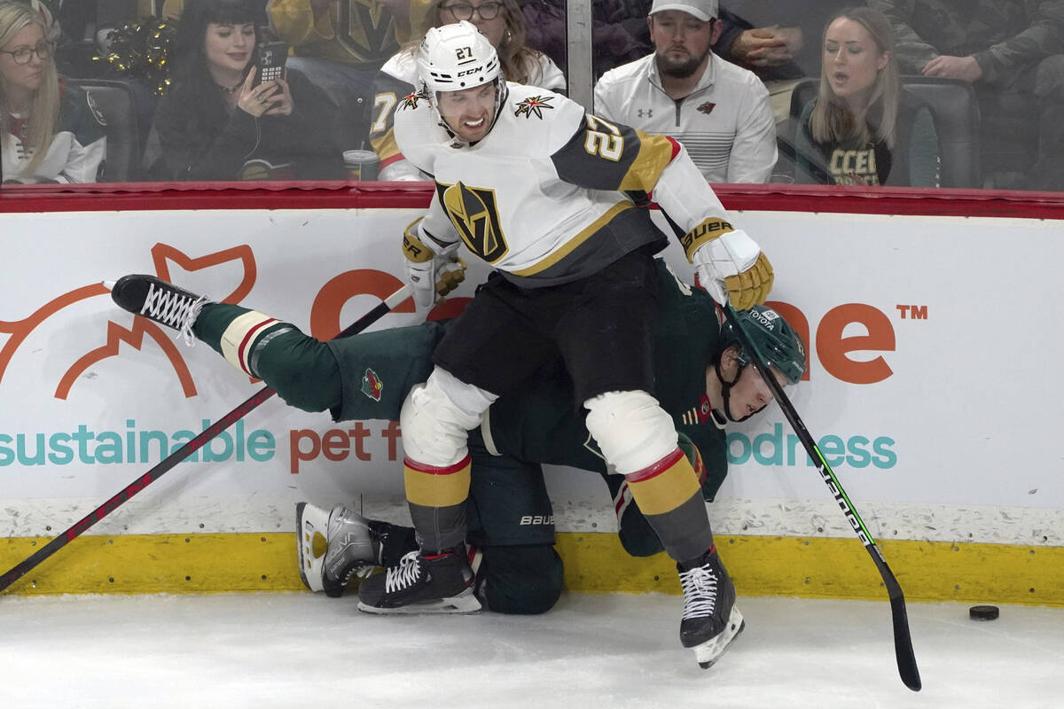 Vegas Golden Knights' Shea Theodore (27) checks Minnesota Wild's Matt Boldy into the boards in ...