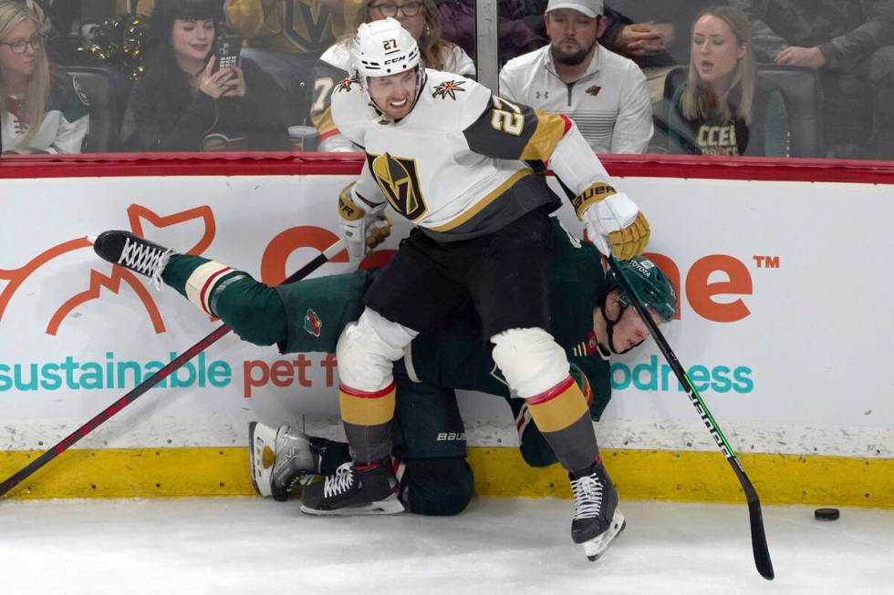 Vegas Golden Knights' Shea Theodore (27) checks Minnesota Wild's Matt Boldy into the boards in ...