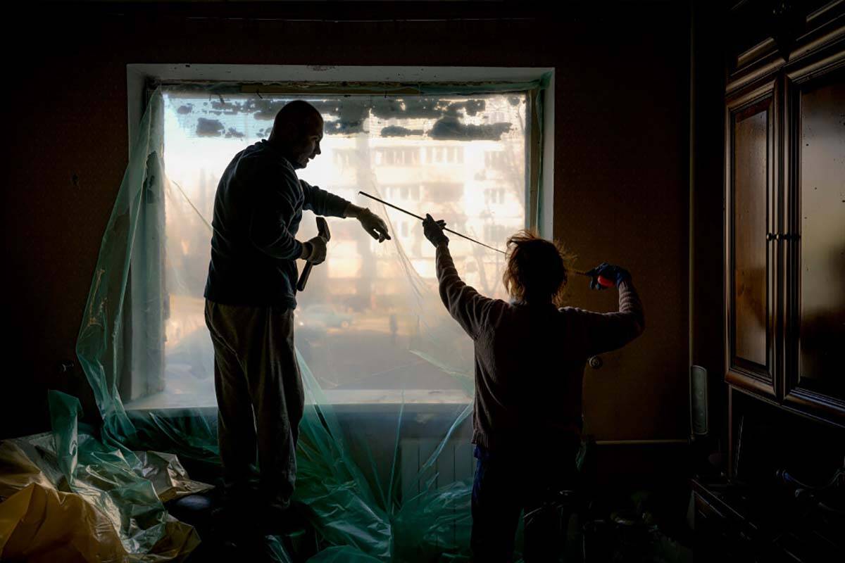 Slava Chikov, left, covers the shattered window of his living room with a plastic sheet in a bu ...