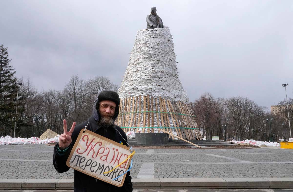 A man holds a poster reading "Ukraine will win" against the background of a monument ...