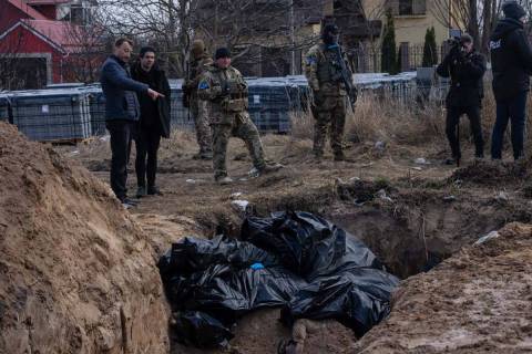 People stand next to a mass grave in Bucha, on the outskirts of Kyiv, Ukraine, Monday, April 4, ...