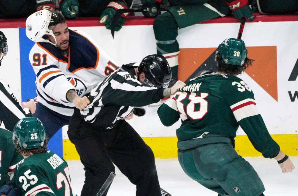 An official, center, gets caught between Edmonton Oilers' Evander Kane (91) and Minnesota Wild' ...