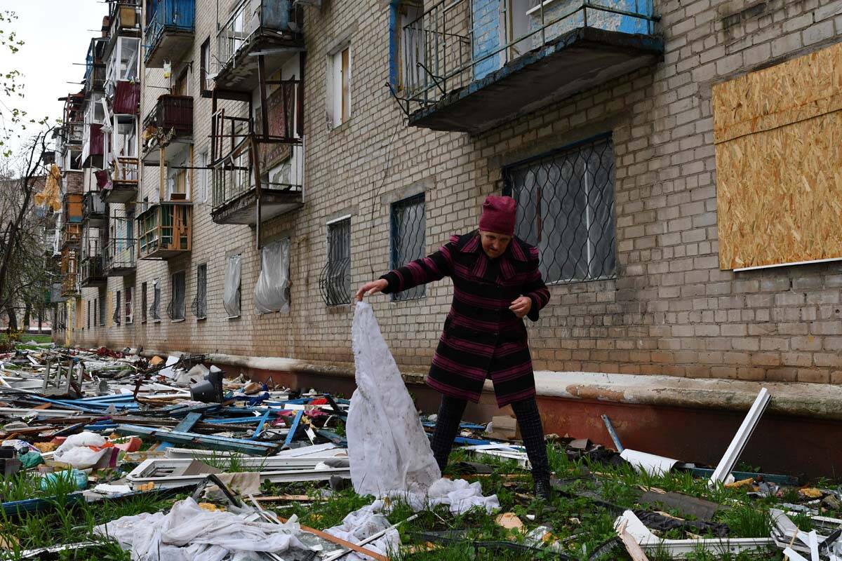 A woman looks for goods dropped from the apartment building partly damaged by shelling, in Kram ...