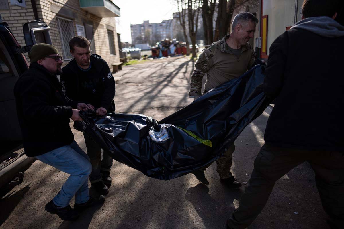 Volunteers carry the body of a man killed during the war to a refrigerated container in Bucha, ...