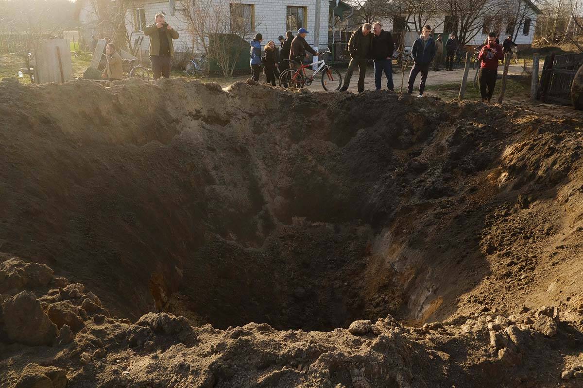 People look at a crater of an explosion in a village of Horodnya, Chernihiv region, Ukraine, Th ...