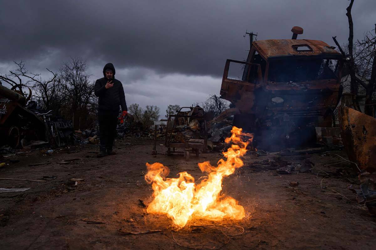 A man takes a photo of burning propellant in a street near destroyed Russian military vehicles ...