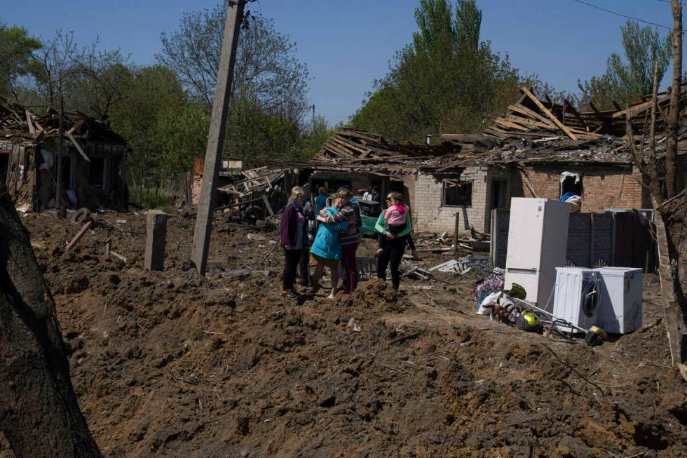 People react as they stand next to a crater in destroyed residential area after Russian airstri ...