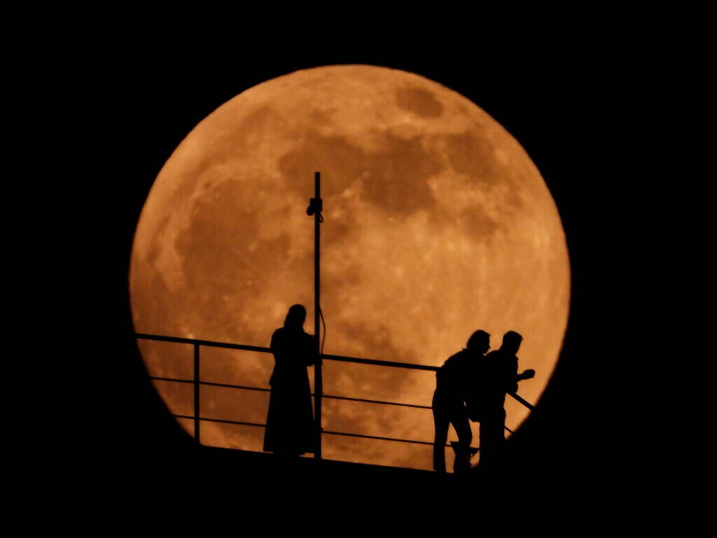 People are silhouetted as an almost full moon rises above the sky in Grozny, Russia, Sunday, Ma ...