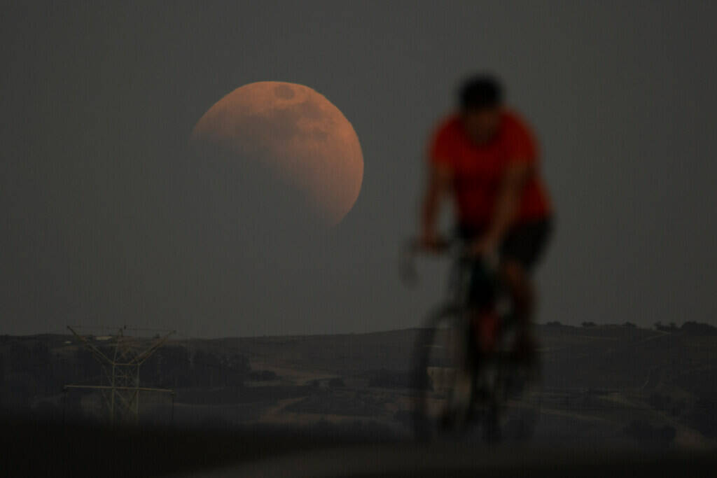 A lunar eclipse is seen behind a cyclist during the first blood moon of the year, in Irwindale, ...