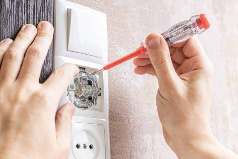 handyman repair wall light switch at apartment. worker using voltage electric tester pen to che ...