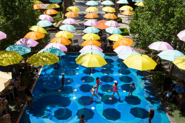 Small umbrellas are hung over a splash pad as children cool themselves at The District on Thurs ...