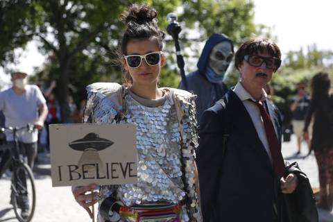 A woman holds a banner with an UFO painted on it and reading "I believe" as another protester d ...