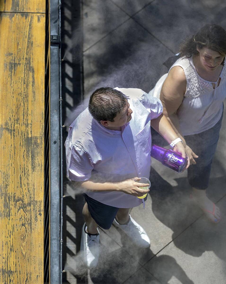Pedestrians enjoy the water misters near Beer Park on a hot day while walking the Las Vegas Str ...