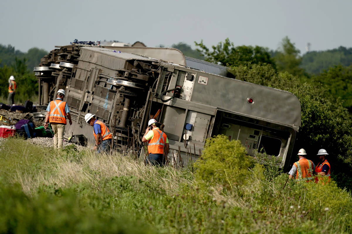 Workers inspect the scene of an Amtrak train which derailed after striking a dump truck Monday, ...