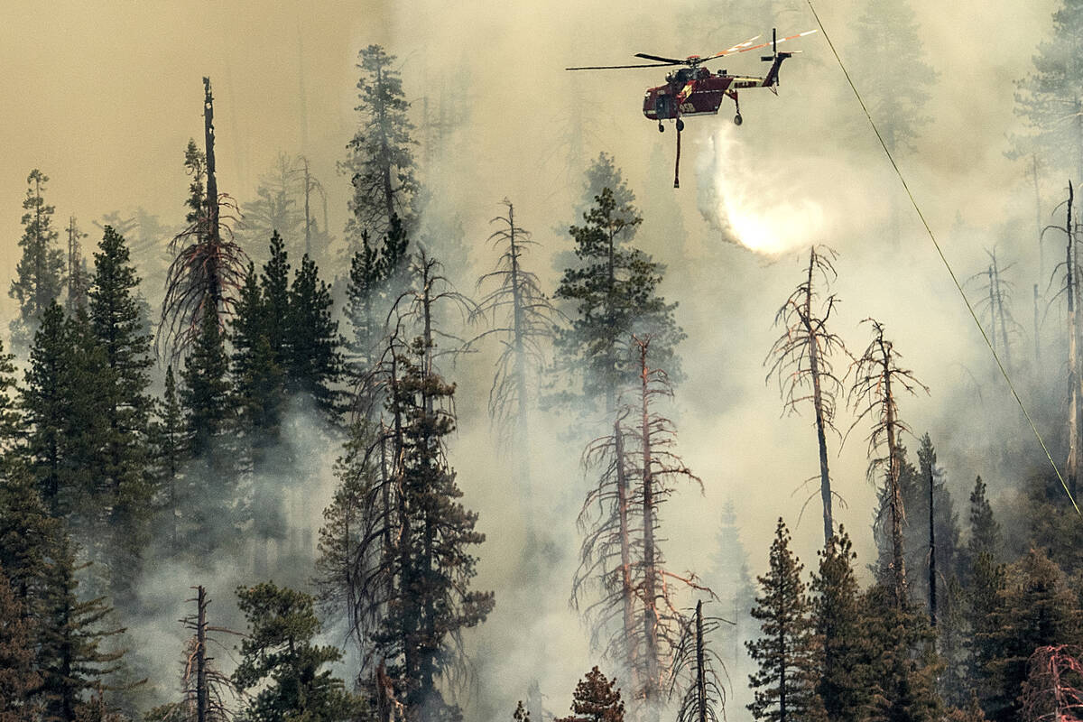 Seen from unincorporated Mariposa County, Calif., a helicopter drops water on the Washburn Fire ...
