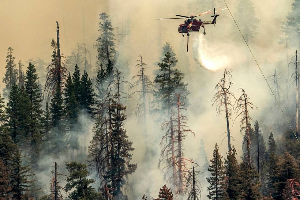 Seen from unincorporated Mariposa County, Calif., a helicopter drops water on the Washburn Fire ...