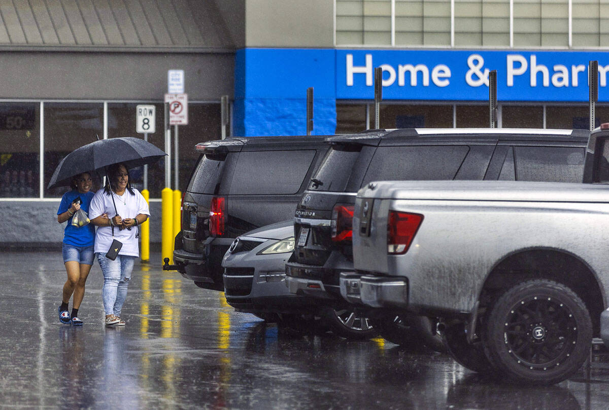 Shoppers take cover beneath an umbrella in a Walmart parking lot as rain moves through the vall ...